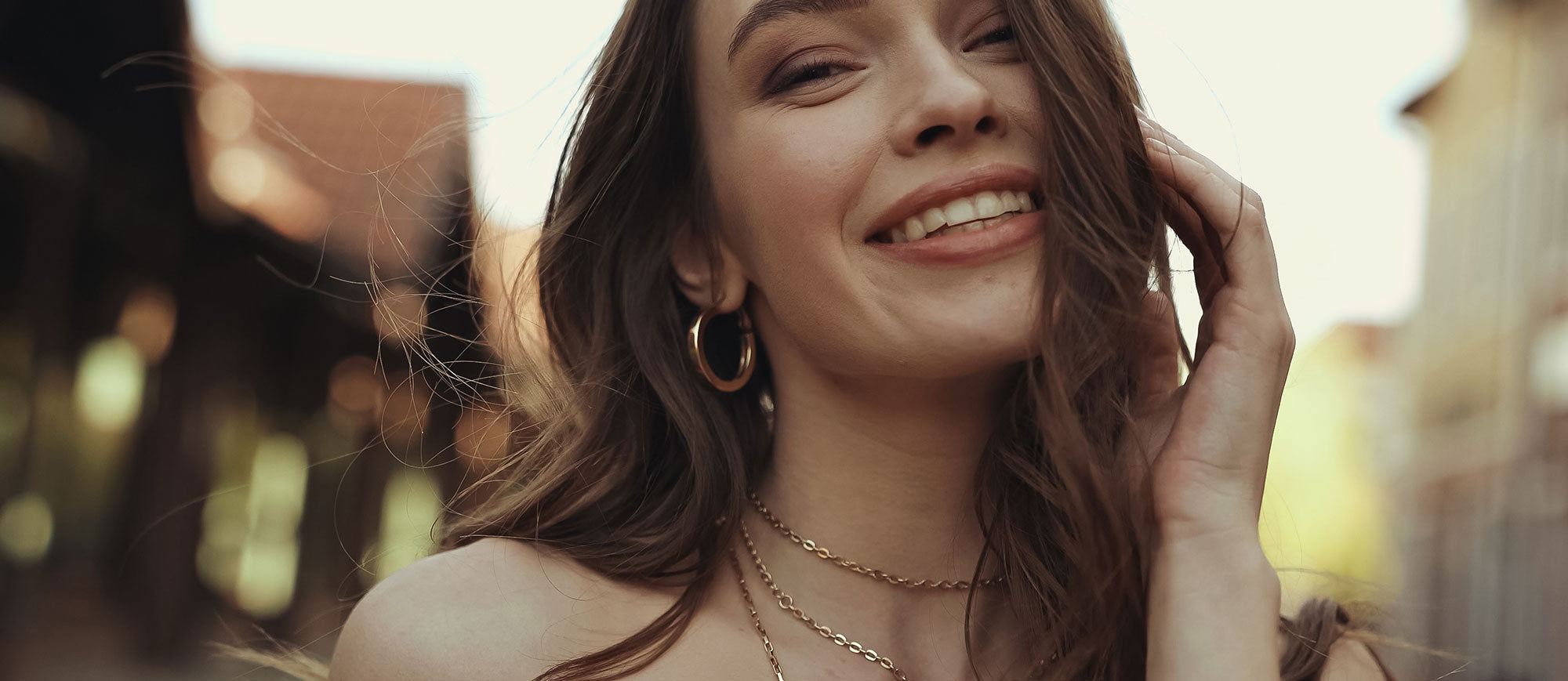 A young woman with dark hair wears golden hoop earrings and few necklaces in a layering look.