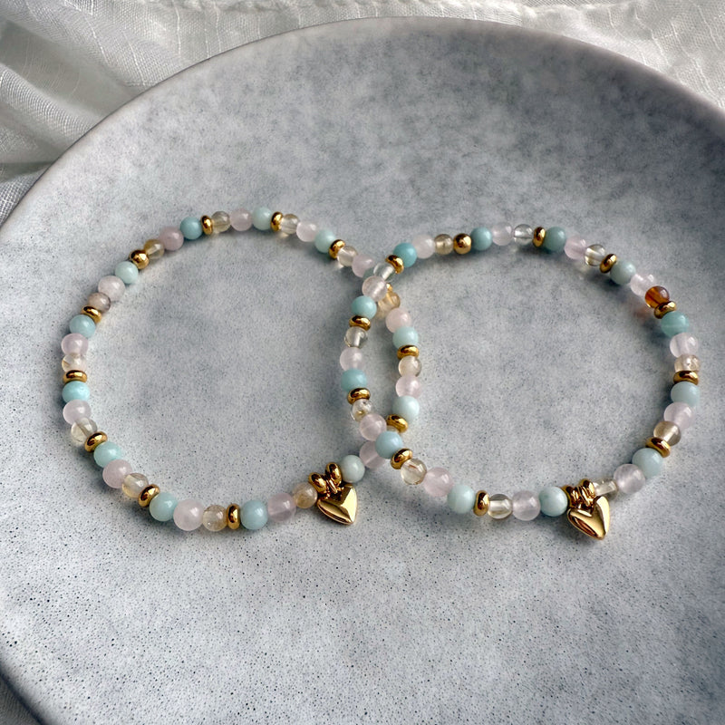 Pair of Sisterhood Bracelets made of citrine, rose quartz, amazonite, and golden spacer beads with heart charm, styled on ceramic plate.