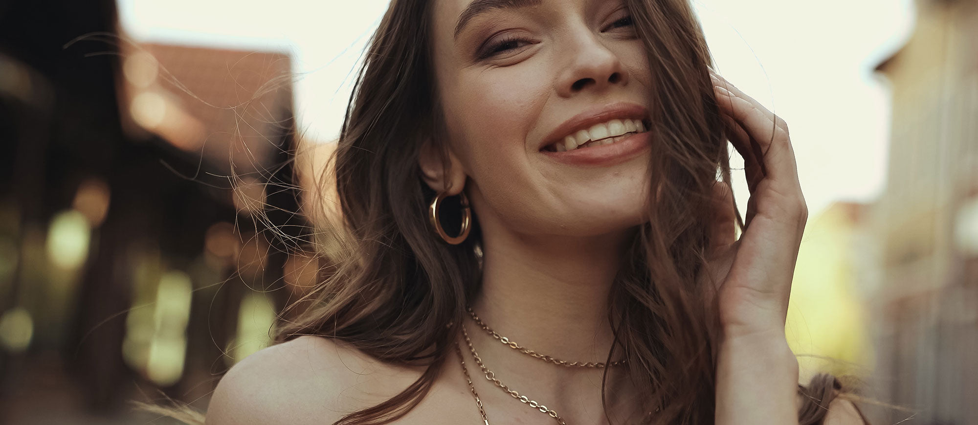 Young woman with brunette hair wears three golden necklaces of different lengths.