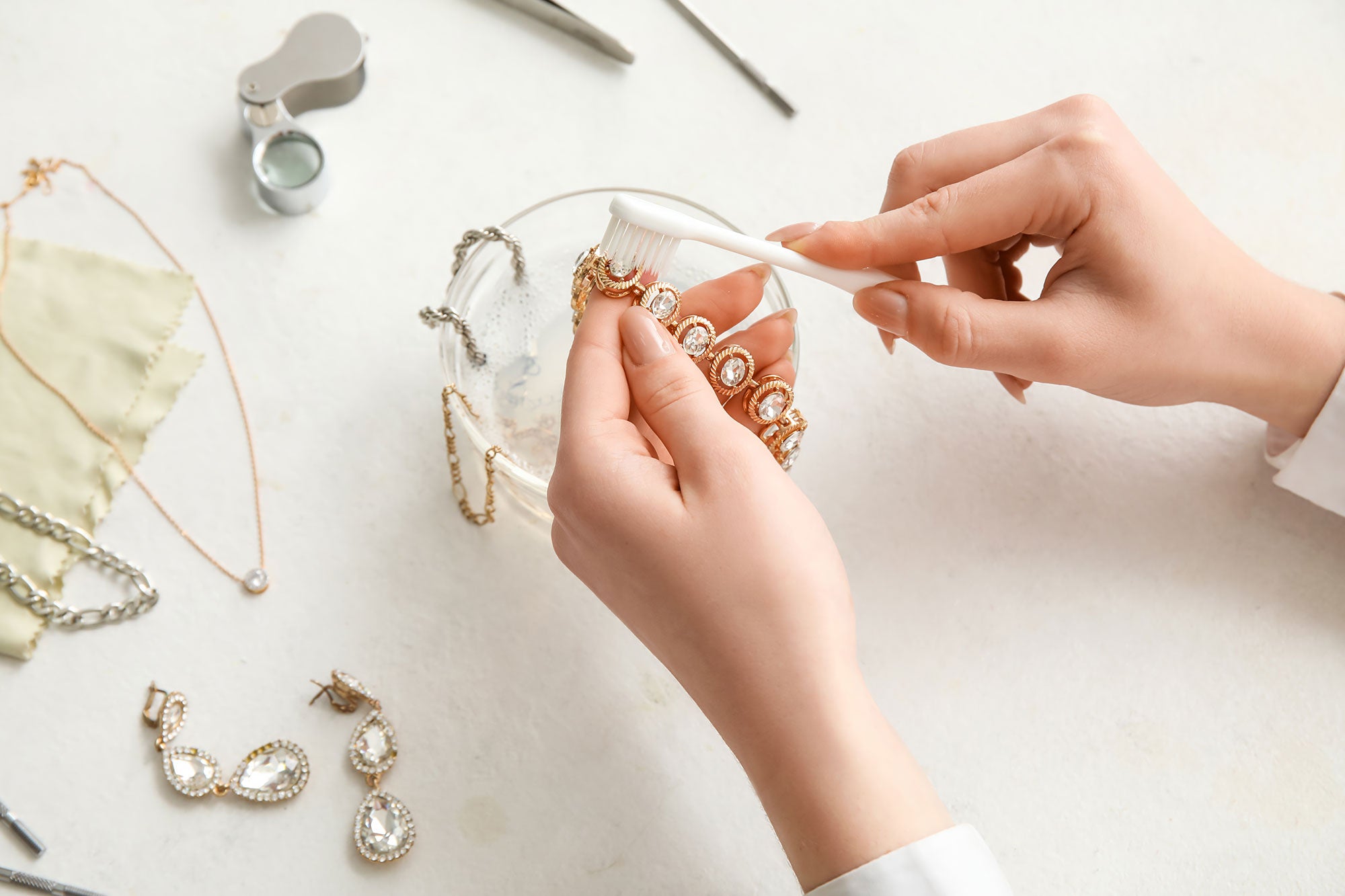 Woman cleaning beautiful bracelet with toothbrush on light background, closeup