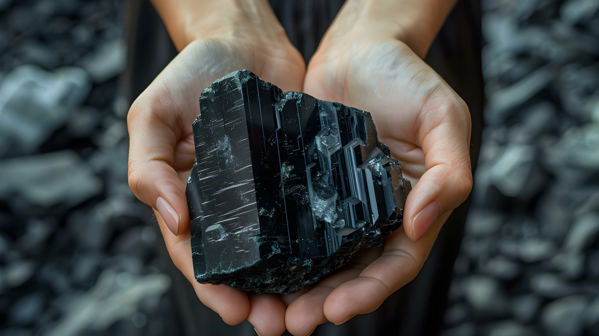 Hands are formed to a bowl and hold a big raw Tourmaline gemstone.