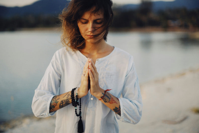 A woman with her hands in prayer pose has a Mala wrapped around her wrists.