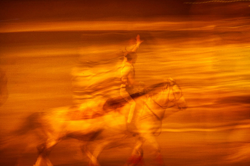 Blurry horse and rider in fiery orange tones representing the energy of the Year of the Fire Horse, symbolizing movement and strength.