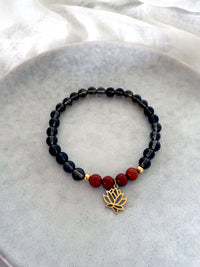 Chakra bracelet made with smoky quartz and red jasper beads, featuring a gold-plated lotus charm and gold accents, handmade by Moksha Jewelry and displayed on a neutral stone background.