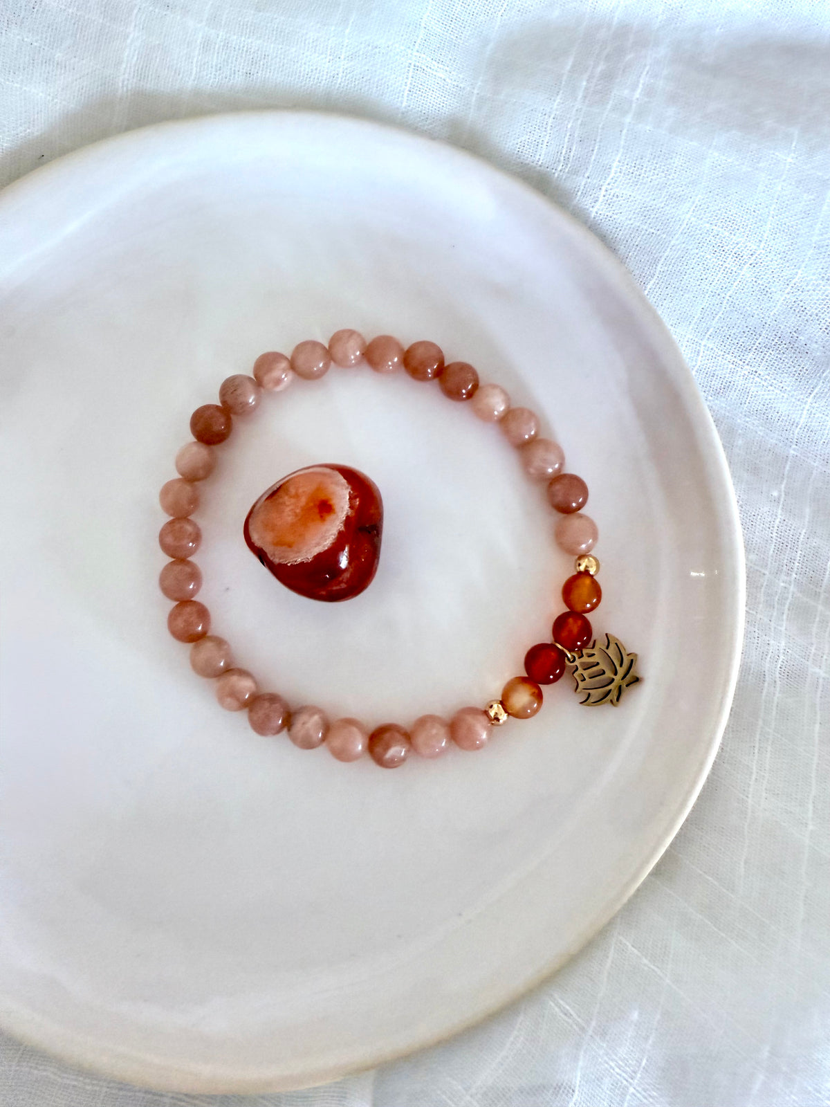 Handmade sacral chakra bracelet crafted with peach moonstone and carnelian beads, accented with gold details and a lotus charm, displayed in soft natural light on a neutral background—designed by Moksha Jewelry to inspire passion, joy, and emotional balance.