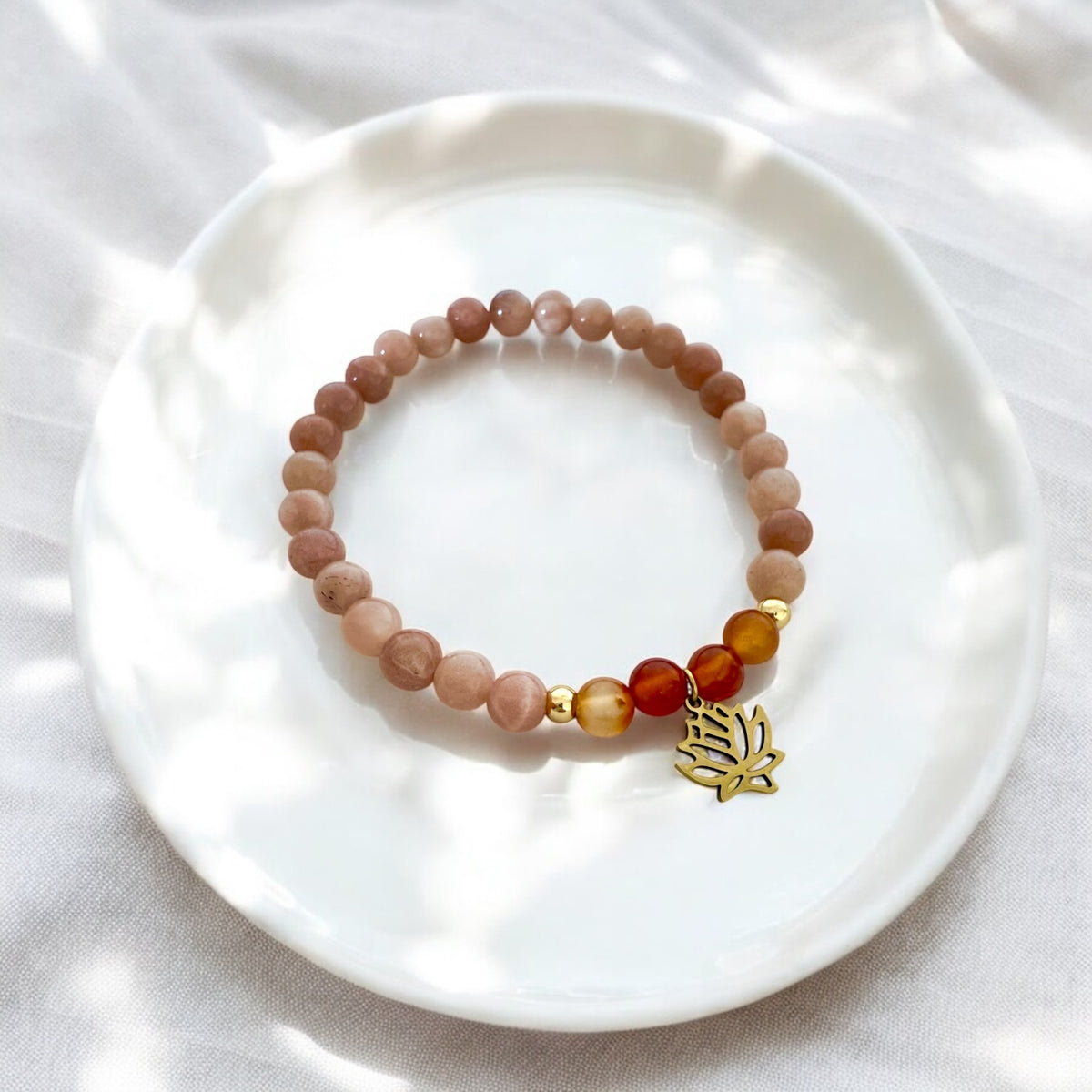 Peach moonstone and carnelian chakra bracelet with gold-plated lotus charm, handcrafted by Moksha Jewelry and styled on a white ceramic plate with soft natural light, designed to activate the sacral chakra and promote joy and creative energy.