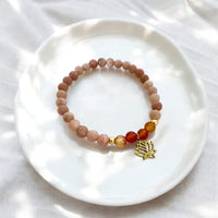 Peach moonstone and carnelian chakra bracelet with gold-plated lotus charm, handcrafted by Moksha Jewelry and styled on a white ceramic plate with soft natural light, designed to activate the sacral chakra and promote joy and creative energy.