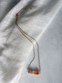 A fine golden necklace with 2 carnelian beads, 2 moonstone beads and one golden bead in the middle on a light fabric. 