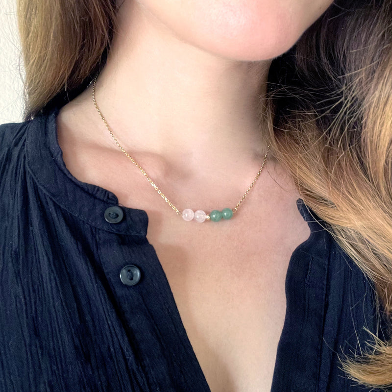 A women wears a fine golden necklace with 2 rose quartz beads, 2 green aventurine beads and one golden bead in the middle.