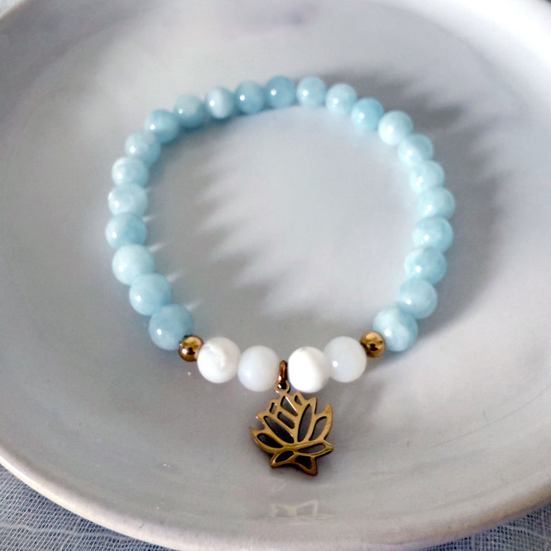 “I Speak My Truth” bracelet by Moksha Jewelry, featuring aquamarine and white opal beads with gold-plated accents and a lotus charm, displayed on a white ceramic dish—designed to support the throat chakra and encourage authentic communication and creativity.