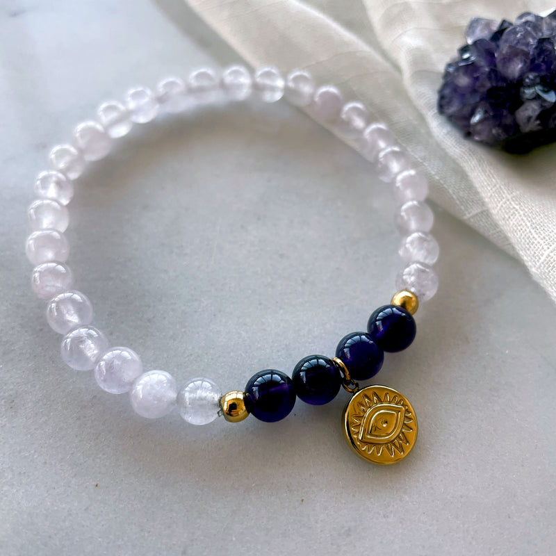 A bracelet made of lavender Amethyst and Amethyst beads, 2 small golden beads with a golden evil eye charm on a light fabric with an Amethyst druse.