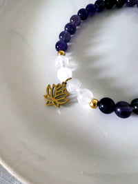Close-up of the “Pure Consciousness” crown chakra bracelet by Moksha Jewelry, featuring polished amethyst and clear quartz beads with a gold-plated lotus charm, styled on a white ceramic plate—symbolizing spiritual awareness, clarity, and energetic harmony.
