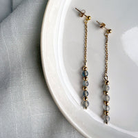 Minimalist product photo of Moksha Jewelry Aurora Drops dangle earrings made with gold-filled posts and labradorite beads, arranged on a white plate with soft natural lighting.