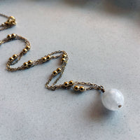 A close-up of a gold plated necklace with a 10mm blue Moonstone bead on a delicate chain with 3mm Ball and 1mm Curb Chain on a ceramic plate.