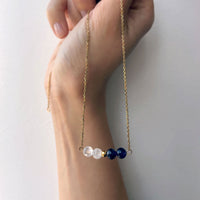 A hand holds a fine golden necklace with 2 Rock Crystal Quartz beads, one small golden bead and 2 Amethyst beads.