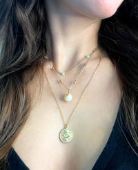 A woman wears a fine gold-plated stainless steel necklace with an Evil Eye pendant with two other necklaces in a layered look.