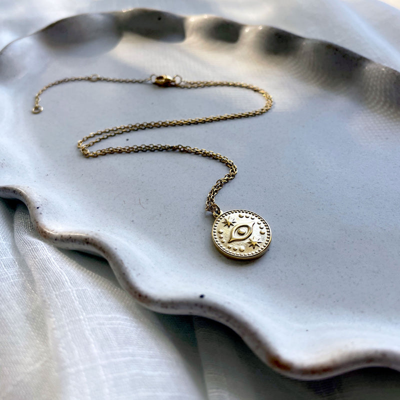 A close-up of a fine gold plated stainless steel necklace with an Evil Eye pendant on a gray ceramic.