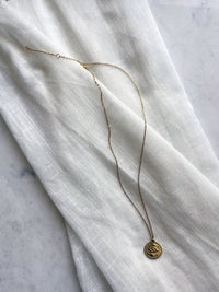 A fine gold plated stainless steel necklace with an Evil Eye pendant on a light fabric.