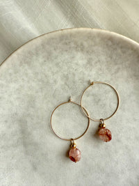 Gold hoop earrings featuring faceted red hematoid quartz gemstones, displayed on a neutral ceramic plate with soft natural lighting — elegant handmade jewelry from the Halo Hoop collection by Moksha Jewelry.