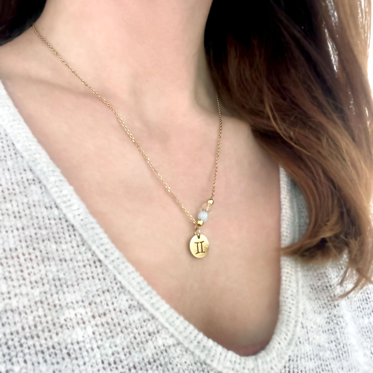 Woman wears a fine golden necklace with a gemini pendant, a Citrine and a Aquamarine bead.