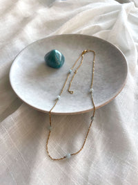 Fine golden necklace with 4mm Amazonite beads on a grey ceramic plate and two Amazonite gemstones.