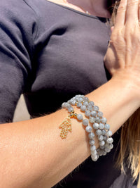 A close-up of a woman who has wrapped a Mala made of Labradorite gemstones and a gold plated Hamsa Hand as a pendant around her wrist.