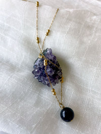 A close-up of a gold plated necklace with a 10mm Amethyst bead on a delicate chain with 3mm Ball and 1mm Curb Chain on a light linen fabric on an Amethyst druse.