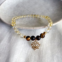 “I Am Strong” chakra bracelet handcrafted with golden citrine and tiger eye beads, featuring a gold-plated lotus charm, styled on a textured white fabric with a stone dish—designed by Moksha Jewelry to activate the Manipura chakra and boost inner strength.