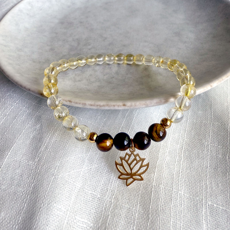“I Am Strong” chakra bracelet handcrafted with golden citrine and tiger eye beads, featuring a gold-plated lotus charm, styled on a textured white fabric with a stone dish—designed by Moksha Jewelry to activate the Manipura chakra and boost inner strength.