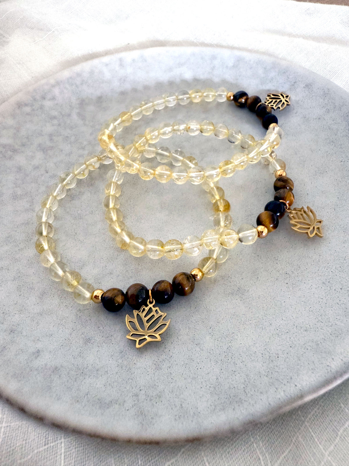 Set of “I Am Strong” chakra bracelets handcrafted by Moksha Jewelry, featuring golden citrine and tiger eye beads with gold-plated lotus charms, displayed on a light stone plate—designed to support personal power, clarity, and Manipura chakra energy.