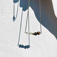 A fine golden necklace with 2 citrine beads, 2 tiger eye beads and one golden bead in the middle in front of a neutral background.