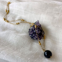 A close-up of gold plated necklace with a 10mm Amethyst bead on a delicate chain with 3mm Ball and 1mm Curb Chain on a light linen fabric on an amethyst druse.