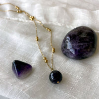 A close-up of a gold plated necklace with a 10mm Amethyst bead on a delicate chain with 3mm Ball and 1mm Curb Chain on a light linen fabric.