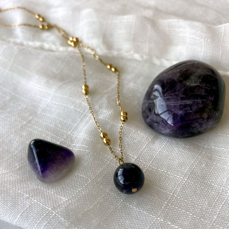 A close-up of a gold plated necklace with a 10mm Amethyst bead on a delicate chain with 3mm Ball and 1mm Curb Chain on a light linen fabric.