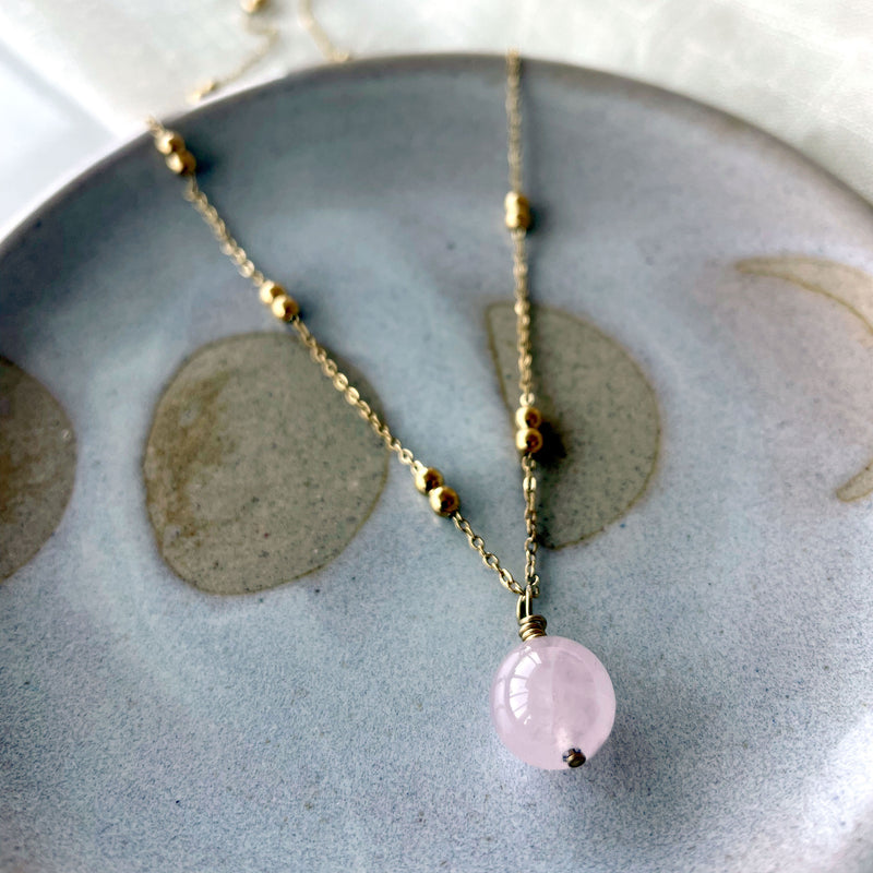 A close-up of a gold plated necklace with a 10mm Rose Quartz bead on a delicate chain with 3mm Ball and 1mm Curb Chain.