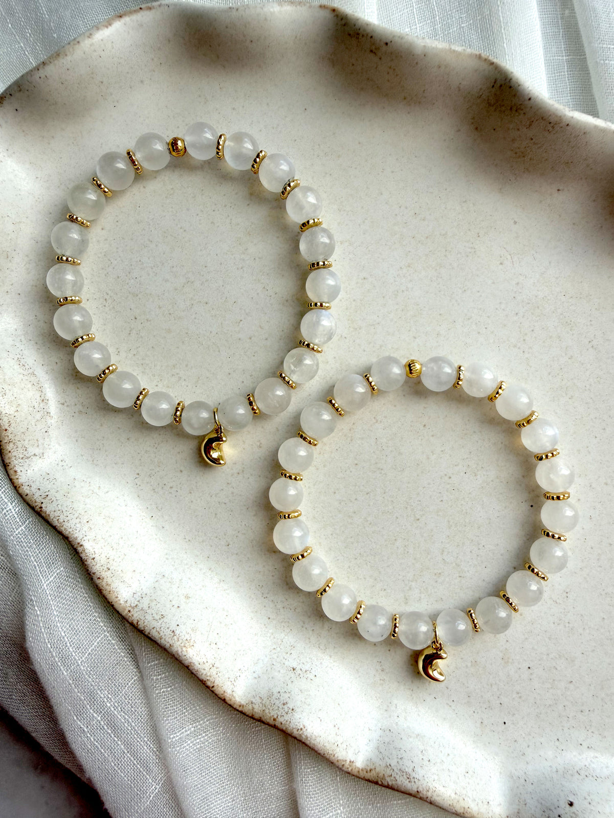 Two handcrafted Lunar Moonstone Bracelets with genuine Moonstone gemstones, gold-plated spacer beads, and crescent moon charms displayed on a ceramic tray.