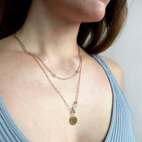 A woman wears a fine golden necklace with 4mm Labradorite beads together with a longer golden Necklace with a gemini pendant and a Citrine and Aquamarine bead.