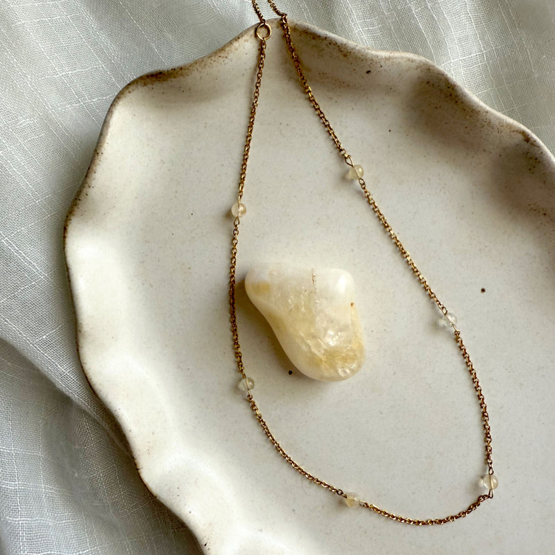 A delicate gold-plated chain with six small 4mm citrine beads, displayed on a ceramic dish, symbolizing abundance and positivity.