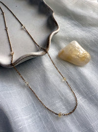 Elegant dainty necklace with fine gold chain and citrine gemstone beads, styled with a natural citrine crystal on soft fabric background.