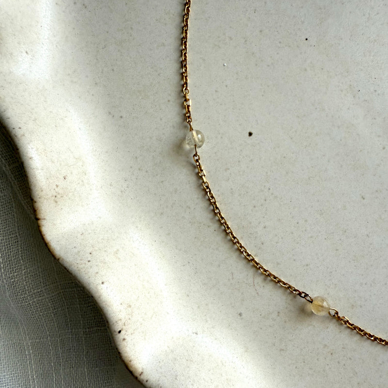 Handmade necklace with subtle golden hues of citrine on a thin chain, styled on a neutral ceramic plate.