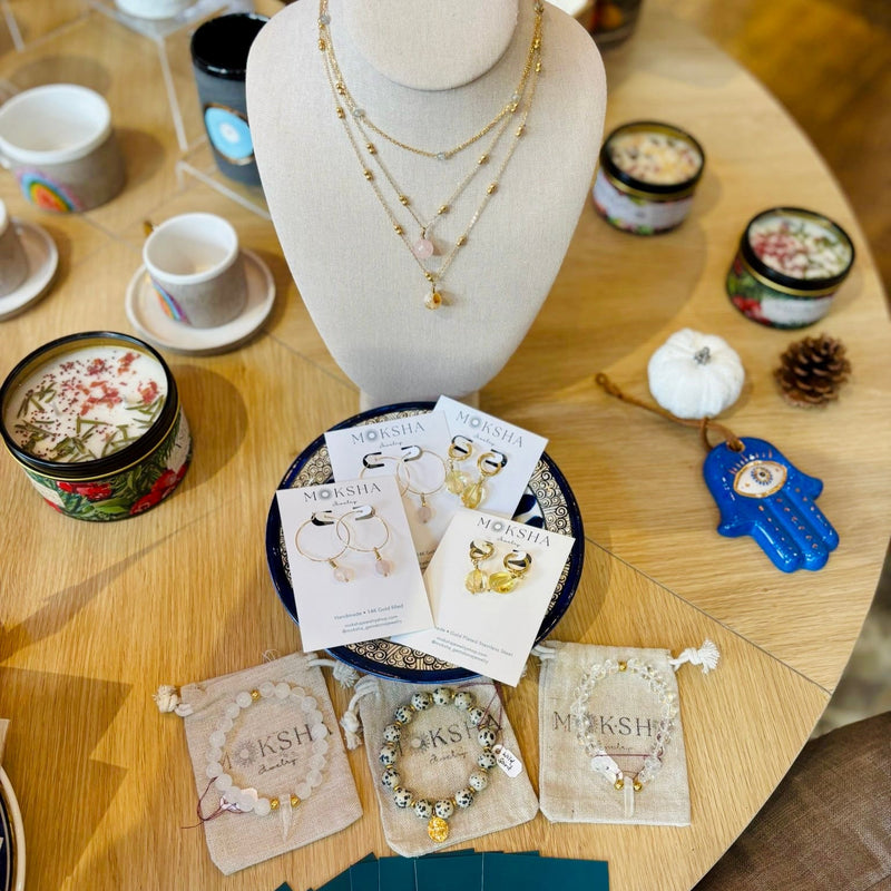 Jewelry display on a mannequin bust with cards and small items on a wooden table.