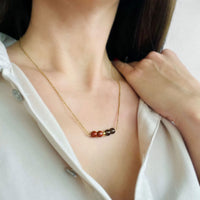 A woman wears a fine golden necklace with 2 red jasper beads, 2 smoky quartz beads and one golden bead in the middle.