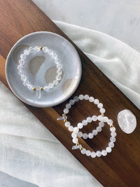 3 Bracelets with 8mm Clear Quartz beads and 3 5x6mm gold plated stainless steel beads and a clear quartz tip focal point on a dark wooden tray.