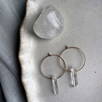 Handmade gold-filled hoop earrings with natural clear quartz point crystals, minimalist gemstone jewelry on ceramic plate.