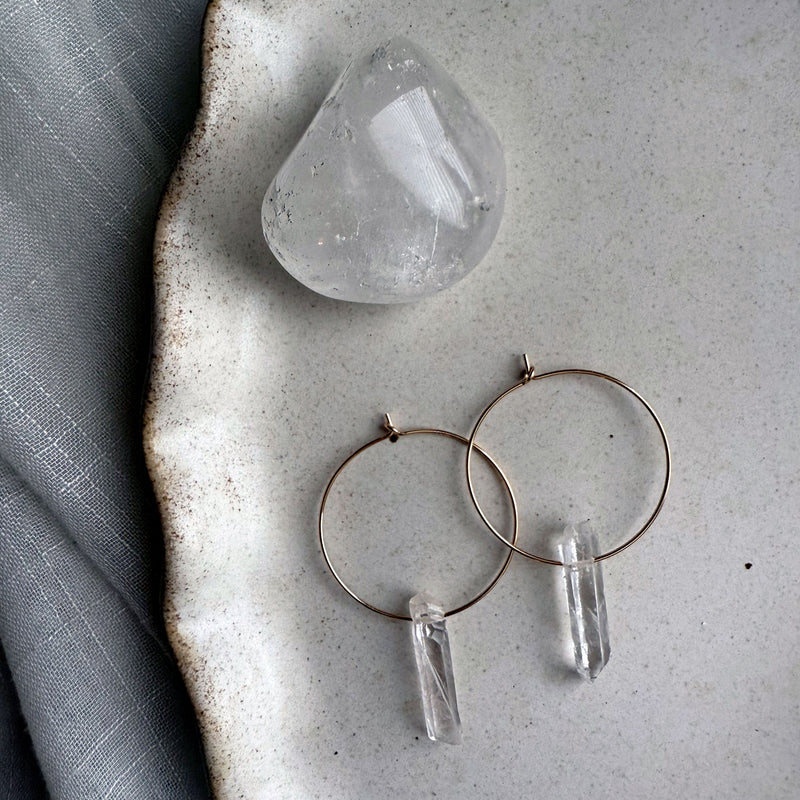 Handmade gold-filled hoop earrings with natural clear quartz point crystals, minimalist gemstone jewelry on ceramic plate.