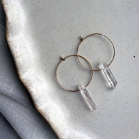Handmade Purity Earrings with clear quartz crystal points on gold-filled hoops, minimalist gemstone hoop earrings on ceramic plate.