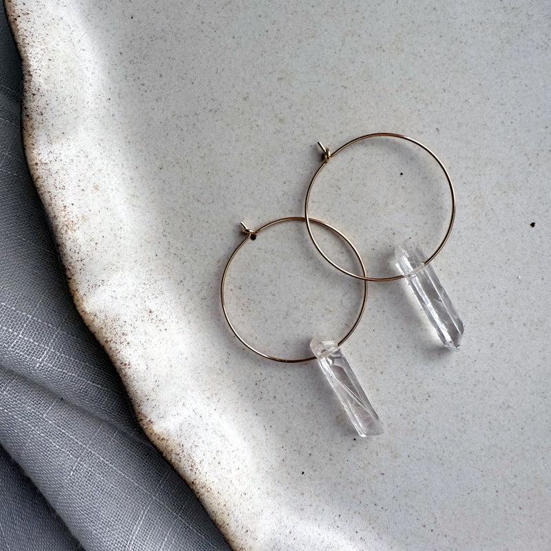 Handmade Purity Earrings with clear quartz crystal points on gold-filled hoops, minimalist gemstone hoop earrings on ceramic plate.
