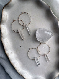 Set of handmade Purity Earrings with clear quartz crystal points on gold-filled hoops, artisanal gemstone jewelry styled on ceramic plate.