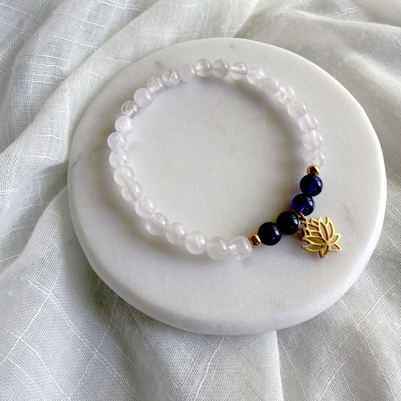 “See Truth Within” bracelet by Moksha Jewelry, featuring amethyst and lavender amethyst beads with clear quartz accents and a gold-plated lotus charm, displayed on a round white marble plate with soft fabric—crafted to support third eye chakra activation, intuition, and inner clarity.
