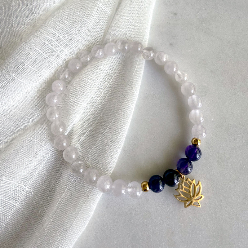 “See Truth Within” third eye chakra bracelet by Moksha Jewelry, handcrafted with lavender amethyst, deep amethyst, and clear quartz beads, finished with a gold lotus charm—displayed on a soft marble surface with light-textured fabric, symbolizing intuition, spiritual clarity, and inner wisdom.